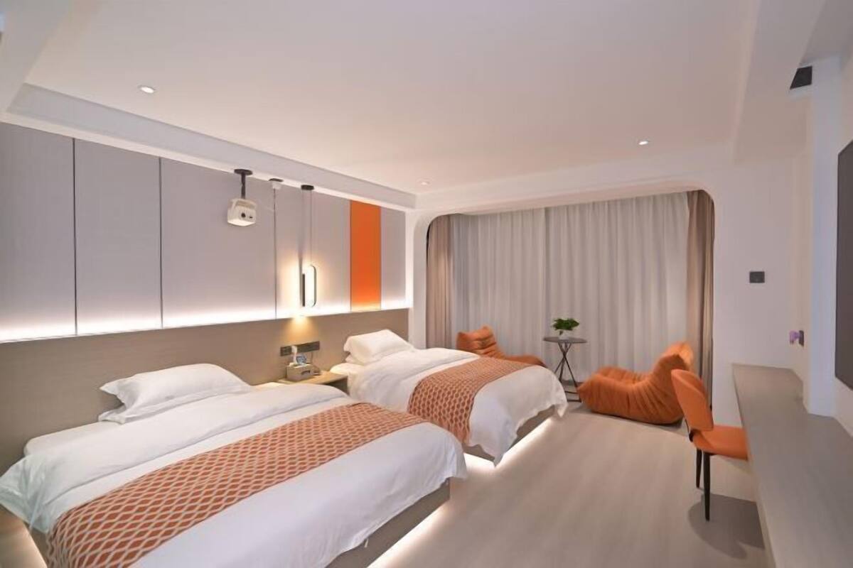 Una habitación de hotel moderna con dos camas, un sofá, una mesita y una ventana con cortinas.