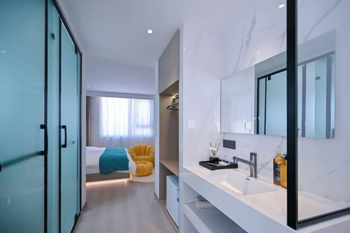 Una habitación de hotel moderna con un espejo grande, un lavamanos blanco y una cama con detalles azules y amarillos.