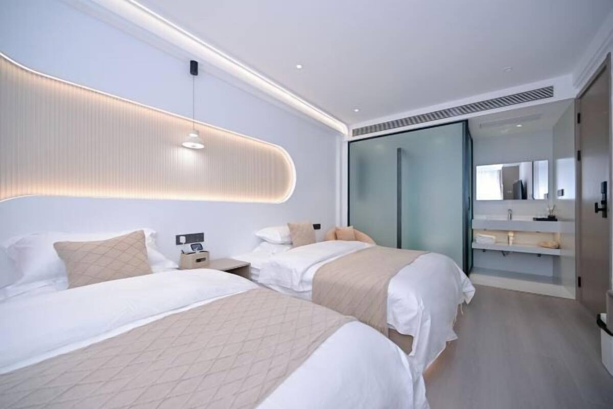 Una habitación de hotel moderna con dos camas, una mesita de noche, un escritorio integrado, cabina de ducha de vidrio y un espejo grande.