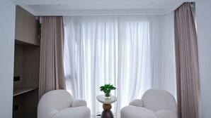 A modern living room with two white armchairs, a small round table with a plant, and a large window with sheer curtains. - Aiqinhai Hotel (Shengsi)