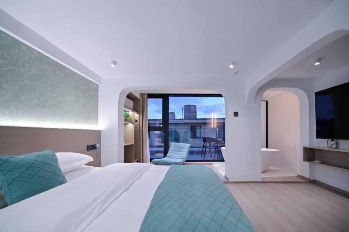 Una habitación de hotel moderna con cama, un pequeño rincón de descanso, televisión y balcón con vistas a la ciudad.