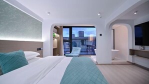 A modern hotel room with a bed, a small seating area, a TV, and a balcony with a city view. - Aiqinhai Hotel (Shengsi)