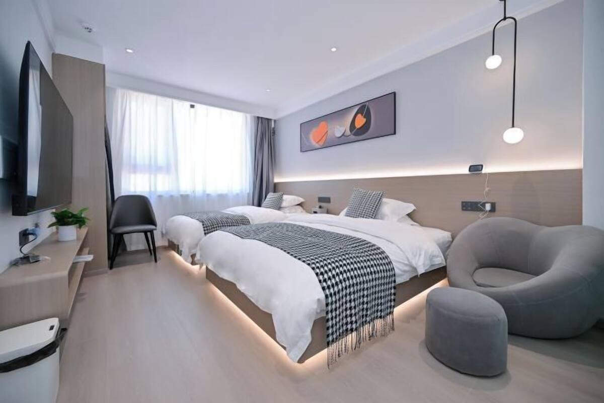 Una habitación de hotel moderna con dos camas, un escritorio con silla, televisión y un amplio ventanal con cortinas.