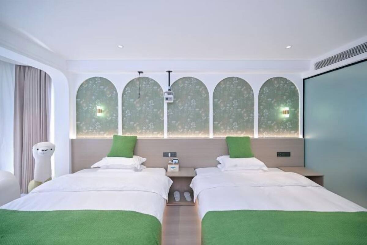 Una habitación de hotel con dos camas, un ventanal con vistas y una pantalla de proyector.