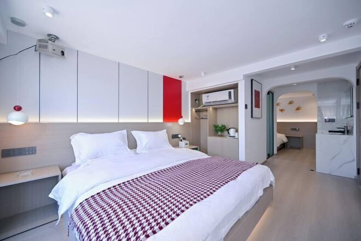 Habitación de hotel moderna con una cama grande, una mesita de noche, televisión integrada y una pared decorada en rojo.