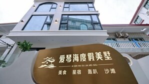 A modern building with a signboard displaying Chinese characters and the name "Ai Qin Hai Du Jia Mei Shu". - Aiqinhai Hotel (Shengsi)