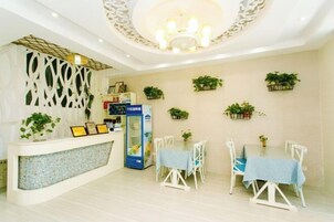 Zona de recepción con mostrador blanco, máquina expendedora azul y mesa de comedor con sillas.