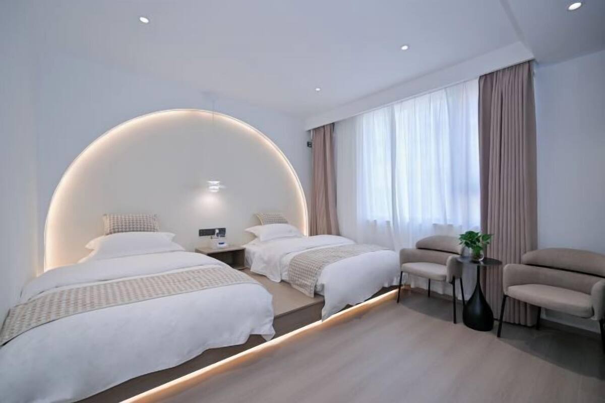 Una habitación de hotel moderna con dos camas, un sofá, una mesita y un ventanal con cortinas.
