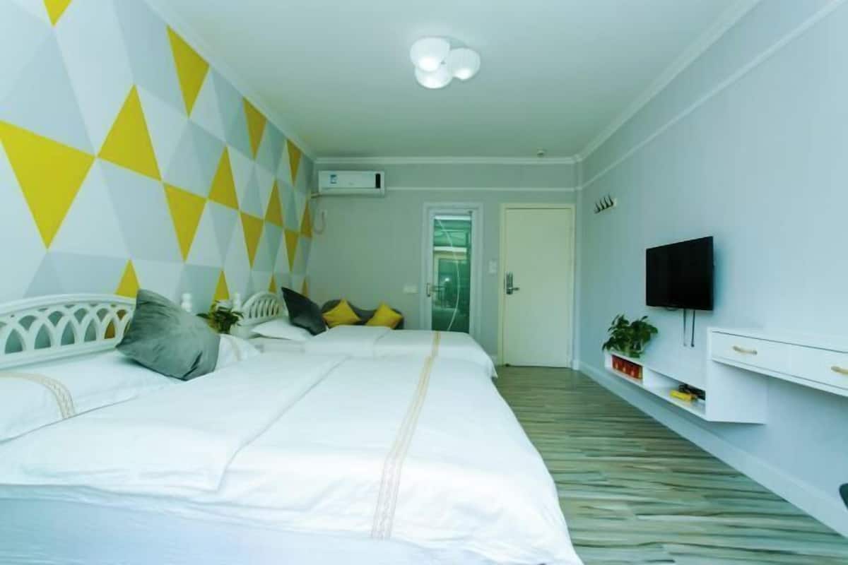 Habitación de hotel con cama, televisor, estante con plantas y puerta que da a otra habitación.