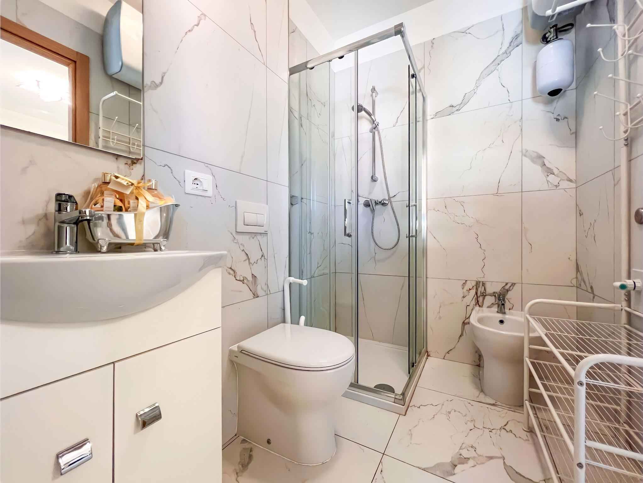 Un bany modern amb plat de dutxa envoltat de vidre, un lavabo blanc i una bassina platejada, i un vàter.