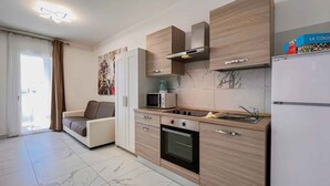 A modern kitchen with wooden cabinets, a microwave, a stove, and a refrigerator. - Studio with balcony and air conditioning (Bibione)
