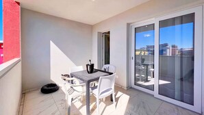 A balcony with a table and chairs, a sliding glass door, and a view of buildings. - Studio with balcony and air conditioning (Bibione)