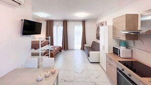 A modern, well-lit room with a bed, a TV, a sofa, a dining table with candles, and a kitchen area. - Studio with balcony and air conditioning (Bibione)