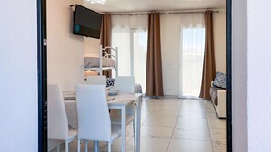 Une chambre d’hôtel moderne dotée d’un coin repas, d’un téléviseur fixé au mur, d’un lit superposé et d’une porte-fenêtre coulissante donnant sur un balcon.