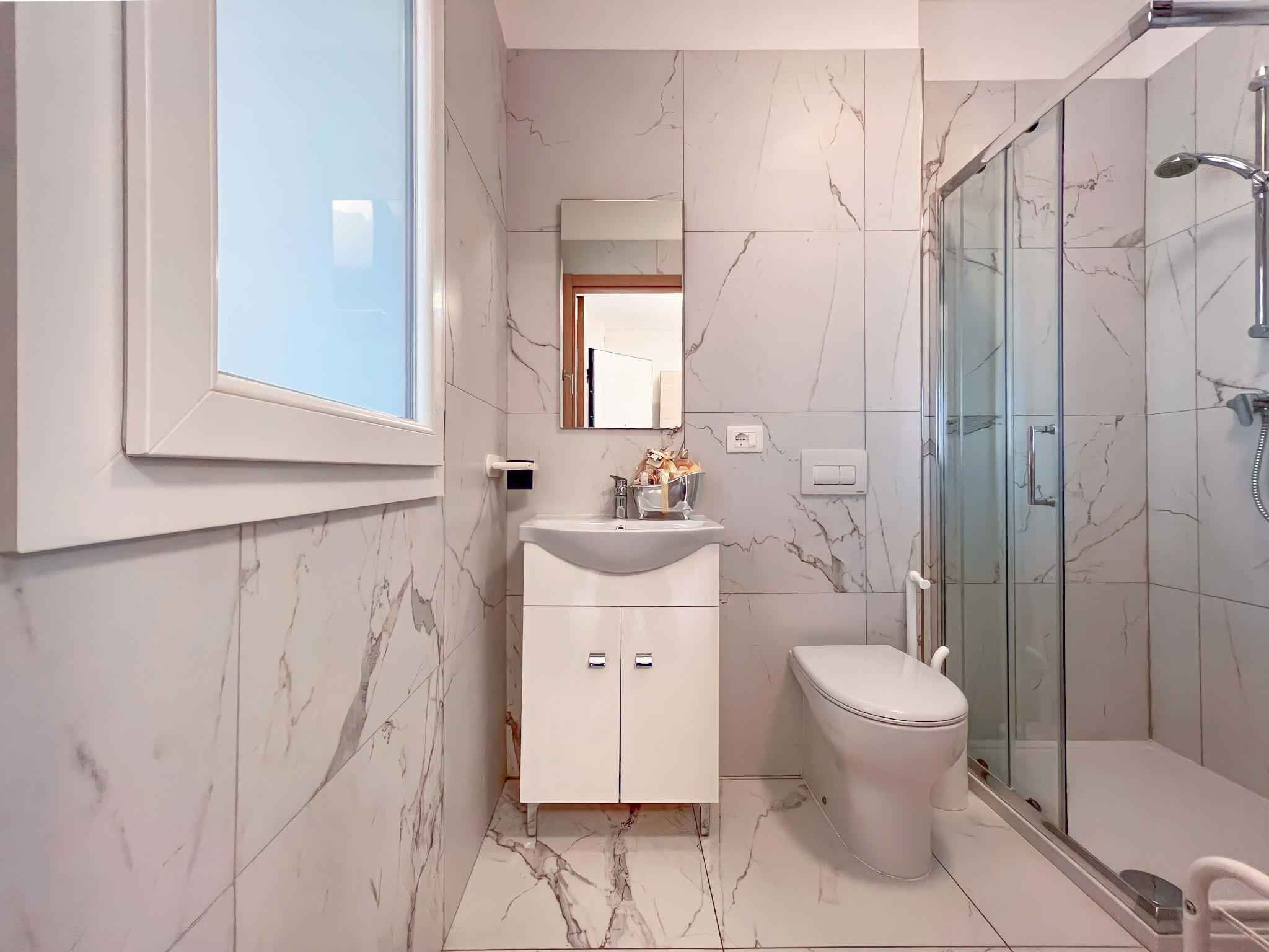 Une salle de bain moderne avec un sol en marbre, un lavabo blanc, des toilettes et une cabine de douche en verre.