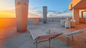 Une terrasse sur le toit offrant une vue sur le coucher du soleil, avec une table, des chaises et une grande colonne.