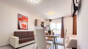 Una sala de estar moderna con un sofá, una mesa de comedor, sillas, un televisor y un cuadro.