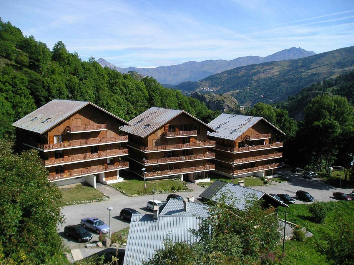 A multi-story wooden building with balconies, surrounded by lush greenery and mountains in the background.