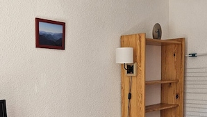 A small, cozy room with a single sofa, a wooden side table, a wall-mounted shelf, and a picture frame. - 1st floor, swimming pool, balcony, tv, ski locker, 32m², Valloire (Valloire)