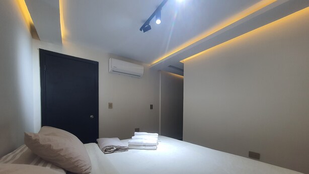 A modern hotel room with a neatly made bed, a dark door, and an air conditioning unit on the wall. - Casa Esther Apartaestudios (Barranquilla)