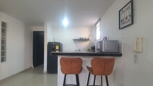 A kitchen with a refrigerator, microwave, and a coffee machine. There are two bar stools and a framed sign on the wall. - Casa Esther Apartaestudios (Barranquilla)