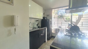 A modern kitchen with white cabinets, a black countertop, a coffee maker, and a refrigerator. - Casa Esther Apartaestudios (Barranquilla)
