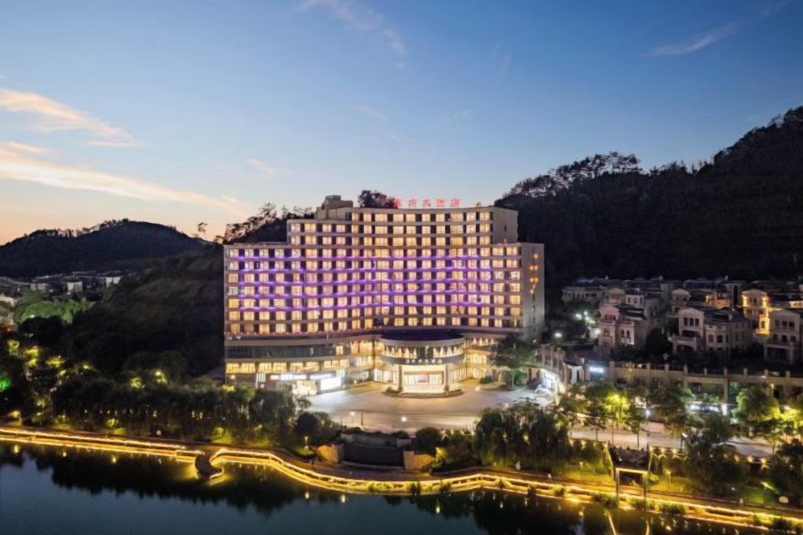 Un hôtel à plusieurs étages doté d’une cour intérieure, entouré d’une étendue d’eau et de collines.