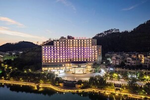 Un hotel de varios pisos con un patio central, rodeado por una masa de agua y colinas.