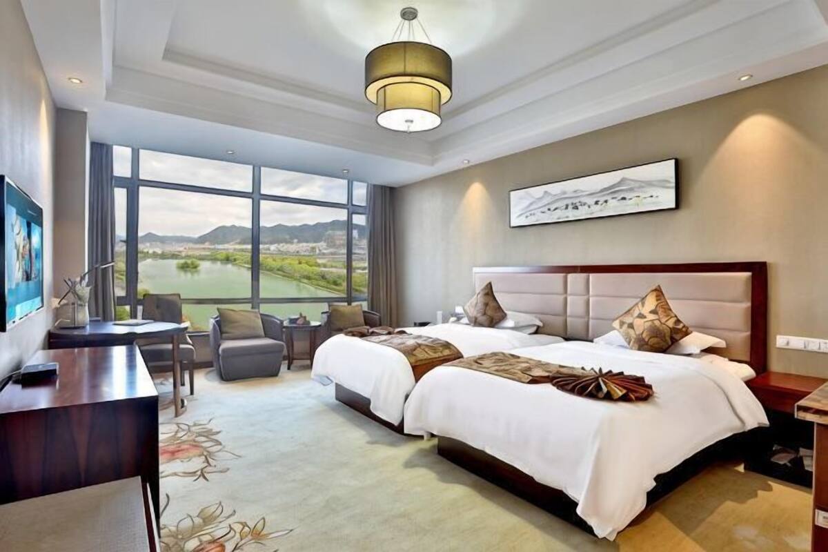 A hotel room with a large bed, a desk, a chair, and a view of a lake.