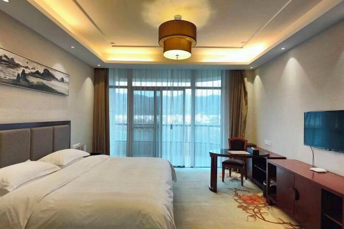 A hotel room with a large bed, a desk with a chair, a television, and a painting on the wall.