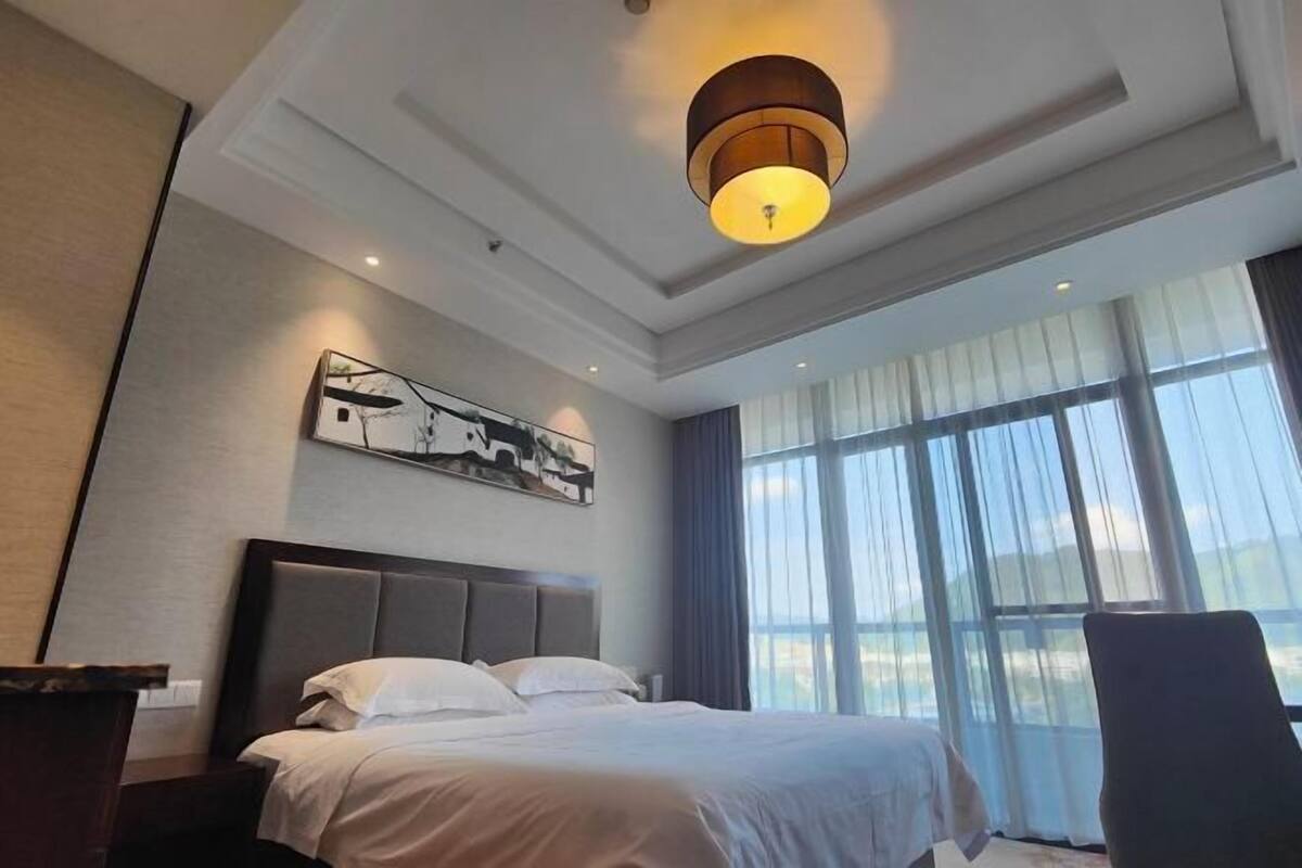 A modern hotel room with a large bed, a desk, and a window with curtains.