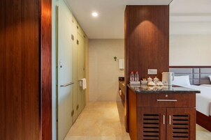 Habitación de hotel con cama, kitchenette pequeña, armario de madera y baño con inodoro y lavamanos.