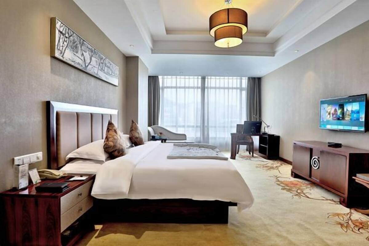 A hotel room with a large bed, a desk, a television, and a window with curtains.