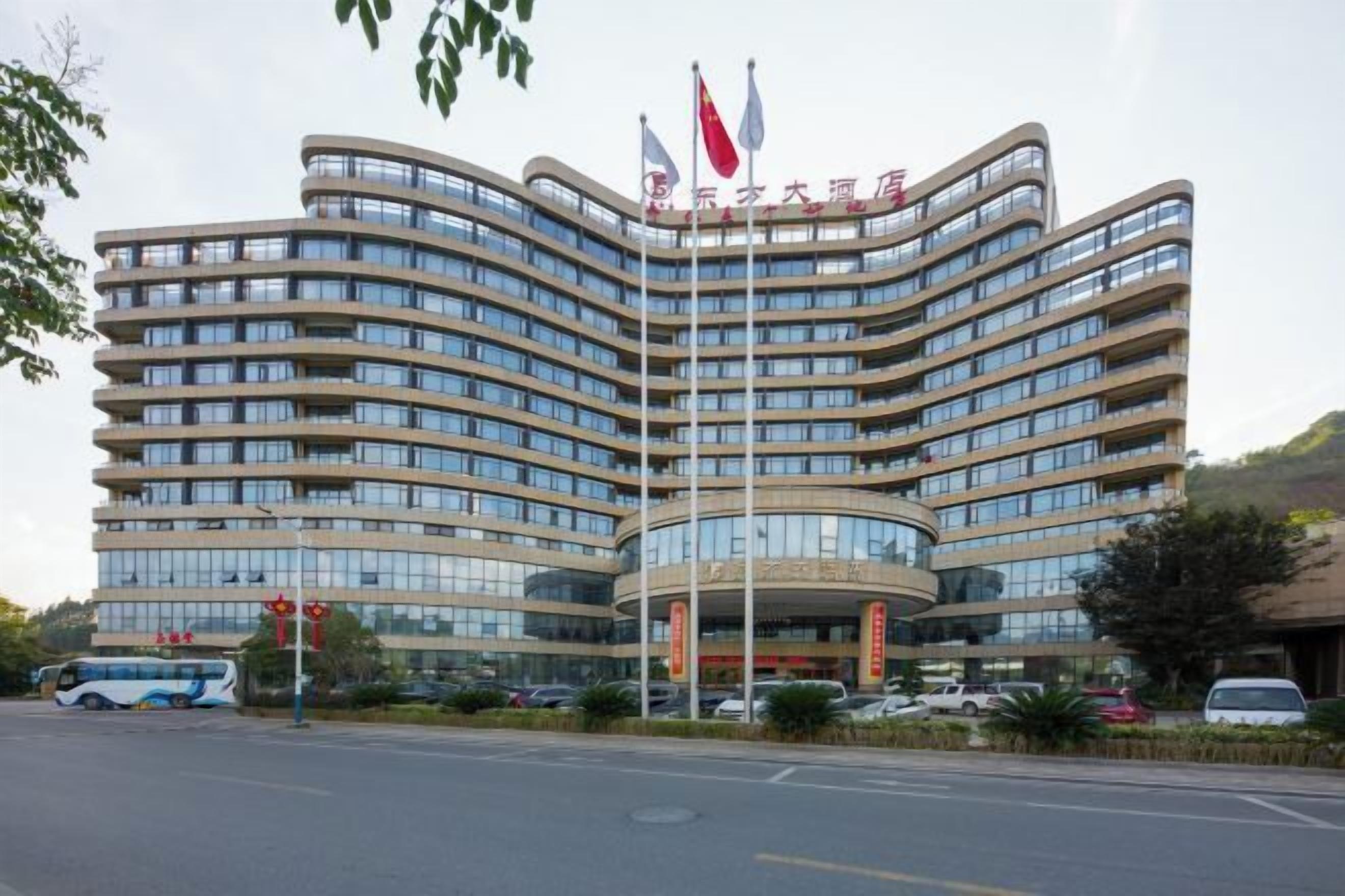 A multi-story hotel with a curved facade, multiple flags, and a parking lot in front.