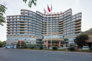 A multi-story hotel with a curved facade, multiple flags, and a parking lot in front. - Oriental Hotel (Kaihua Linhu Road) (Kaihua)