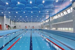 Una amplia piscina interior con varias pistas, techo hexagonal y grandes ventanales a un lado.