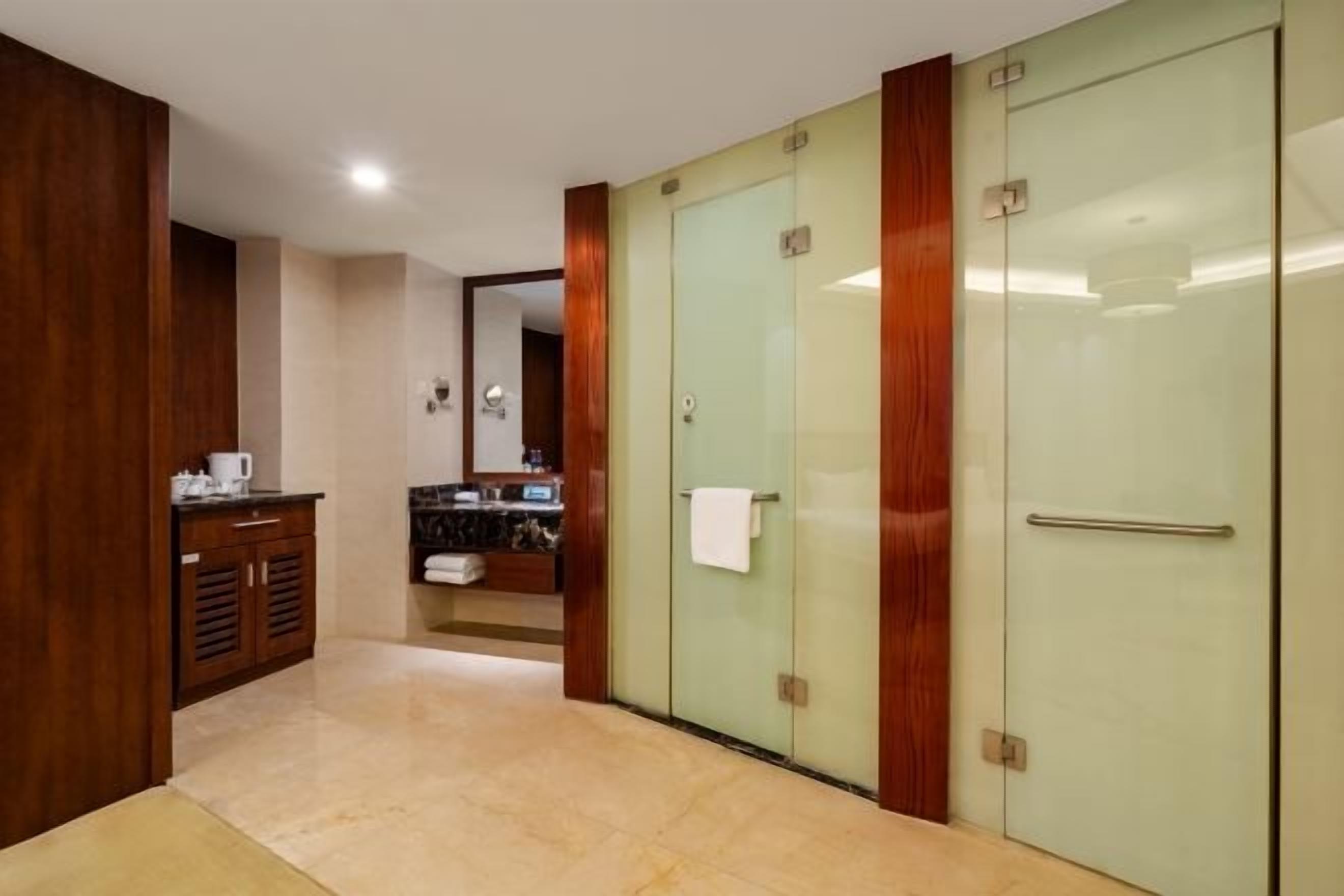 A hotel corridor with a wooden cabinet, a glass door, and a mirror.