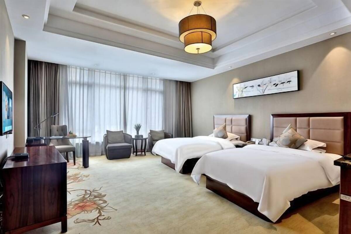 A hotel room with two beds, a desk, a chair, a small table, and a large window with curtains.