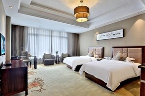 Une chambre d’hôtel avec deux lits, un bureau, une chaise, une petite table et une grande fenêtre avec des rideaux.