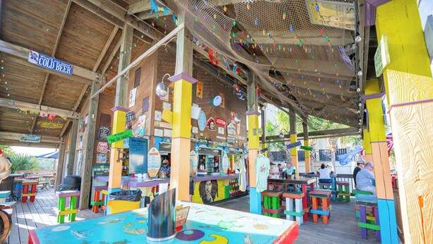 An outdoor restaurant with colorful tables and chairs, a wooden deck, and various signs and decorations. - Island Sunrise HHI Condo (Hilton Head Island)