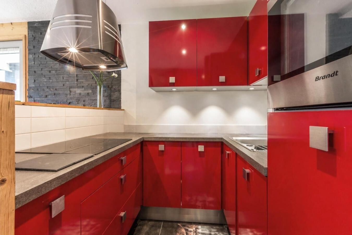 A modern kitchen with red cabinets, a stainless steel range hood, and a built-in oven.
