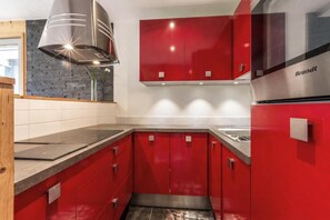 Uma cozinha moderna com armários vermelhos, um exaustor de aço inoxidável e um forno embutido.