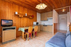 A wooden interior with a dining table, chairs, a television, a microwave, and a sofa.