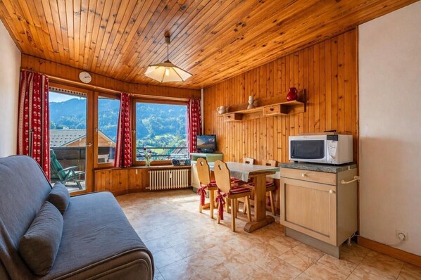 A cozy cabin with a wooden interior, a dining area with chairs, a sofa, a TV, and a microwave.