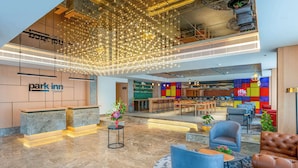 Un hall d’hôtel moderne avec un comptoir d’accueil, un espace salon et un mur aux couleurs vives.