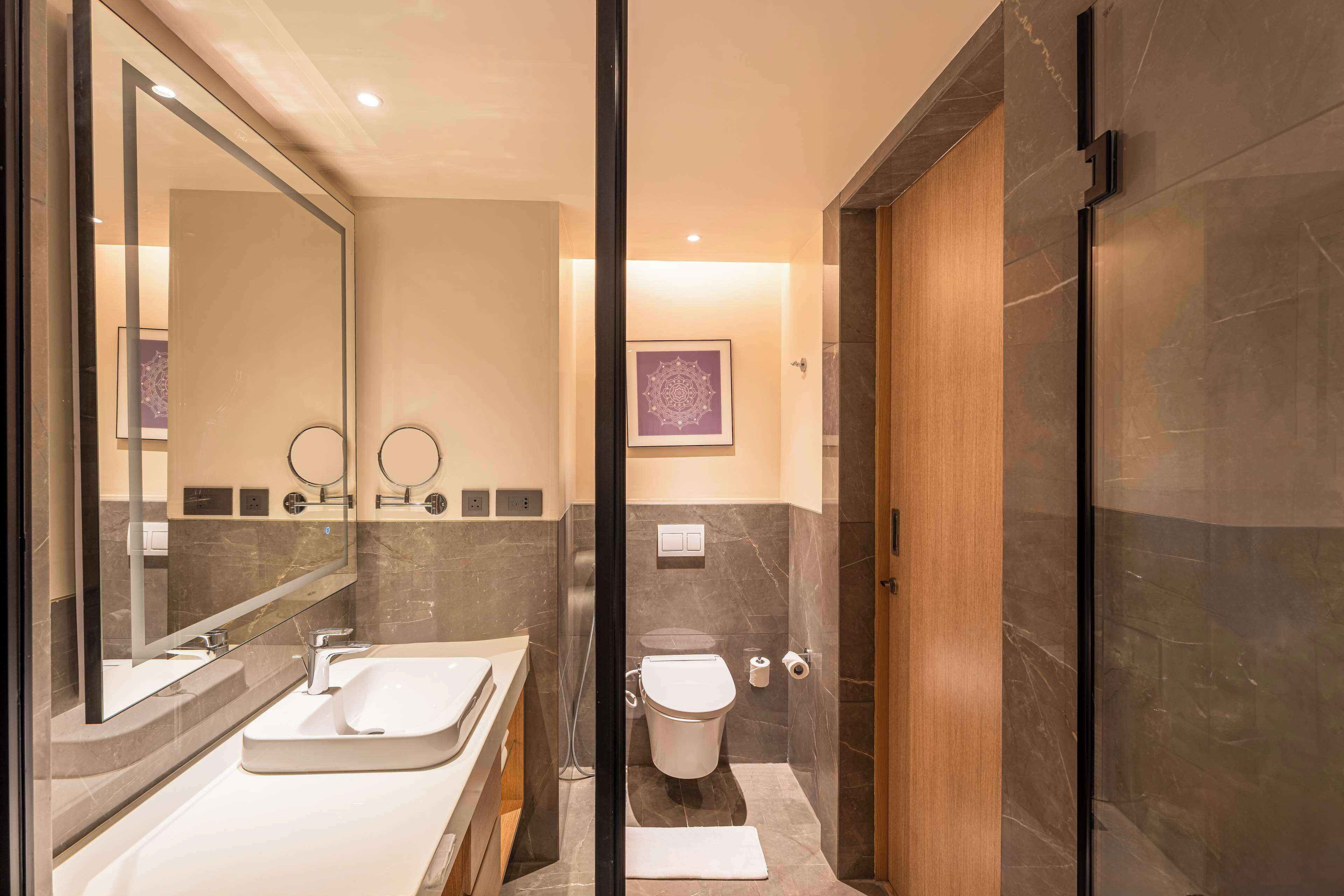 A modern bathroom with a large mirror, two sinks, a toilet, and a shower area.