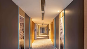 Un long couloir étroit d’hôtel, avec des murs et des portes en bois, un revêtement de sol en moquette et un éclairage encastré.