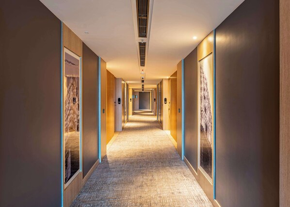 Un long couloir étroit d’hôtel, avec des murs et des portes en bois, un revêtement de sol en moquette et un éclairage encastré.