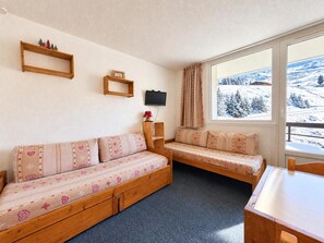 A cozy room with a sofa and a bench, a television, a window with a snowy view, and a small shelf with decorative items.