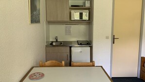 Eine kompakte Küche mit Kühlschrank, Mikrowelle und Spüle. Ein Esstisch mit Stühlen und ein kleines Schrank über der Arbeitsplatte.
